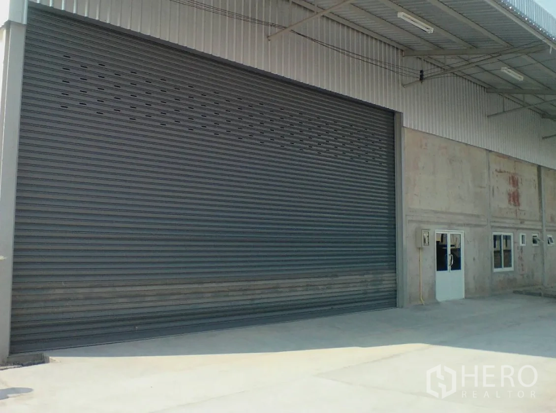 Warehouse for rent in Lam Luk Ka, Pathum Thani - Close-up of extra-wide electric roller shutter door with adjacent personnel door.