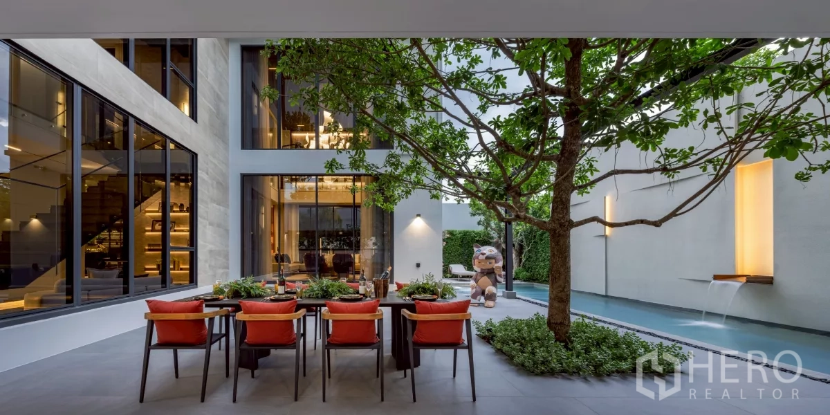 Detached House for rent in Saphan Sung, Bangkok - Private courtyard with outdoor dining under a tree, water feature and long lap pool beside floor‑to‑ceiling windows.