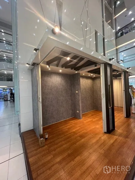 Retail Space for rent - Open-front retail booth with foldable partitions, ceiling lights, and wood floors in a bright mall corridor.