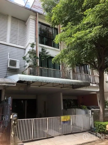 Townhouse for sale - Three-storey townhouse facade with white gate, covered carport, balconies, and a large shade tree.