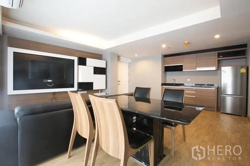 Condominium for rent in Khlong Toei, Bangkok - Dining area with black marble table beside open kitchen and media wall.