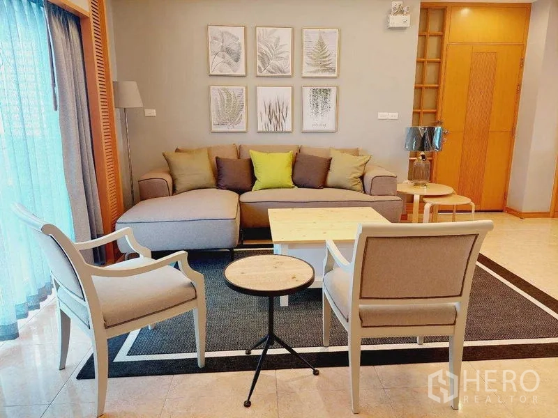 Apartment for rent - Cozy living corner with L-shaped sofa, two armchairs, nesting tables and botanical wall prints.