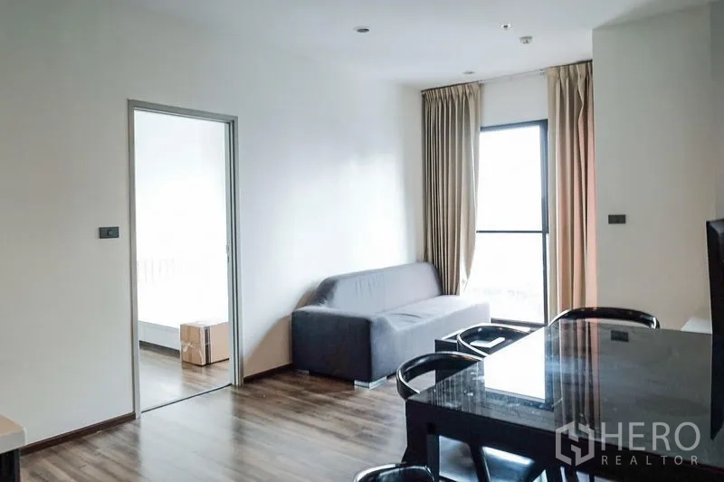 Condominium for rent in Khlong Toei, Bangkok - Open living and dining area with sofa and tall window toward the balcony.