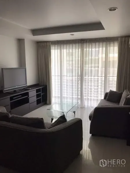 公寓 出租在Watthana, Bangkok - 采光良好的客厅，落地窗纱帘、电视柜、沙发与玻璃茶几，连接阳台。