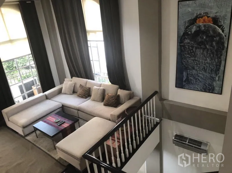 Townhouse for rent in Bang Kapi, Bangkok - High-ceiling living room with a large sectional sofa and tall arched windows.