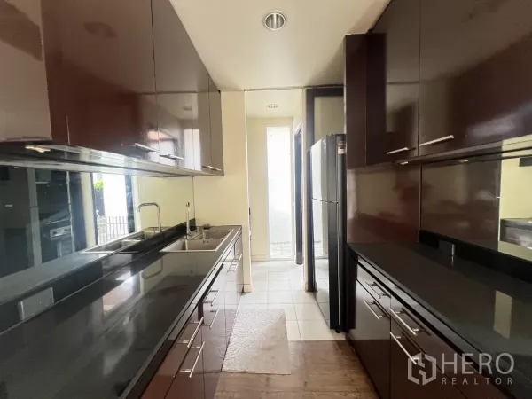 Detached House for rent in Wang Thonglang, Bangkok - Galley kitchen with glossy cabinetry, black countertops and stainless sink.