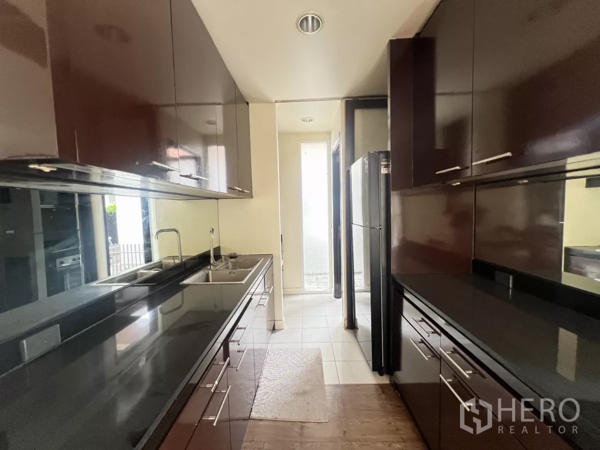 Detached House for rent in Wang Thonglang, Bangkok - Galley kitchen with glossy cabinetry, black countertops and stainless sink.