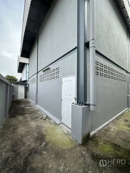 Warehouse for rent in Pak Kret, Nonthaburi - Side walkway along the warehouse with a service door and concrete surface.