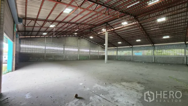 Warehouse for rent in Krathum Baen, Samut Sakhon - Spacious empty warehouse interior featuring a high steel truss roof, skylights, and a concrete floor.