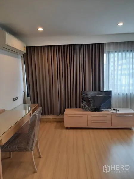 Condominium for rent in Watthana, Bangkok - Living space with TV console, work desk, air conditioning and full-length curtains.