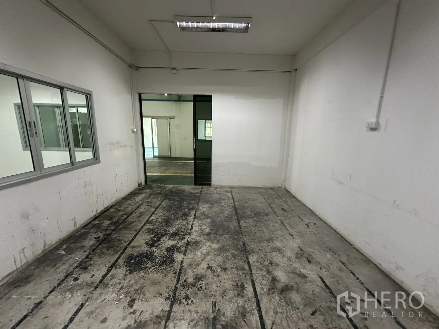 Warehouse for rent in Bang Na, Bangkok - Compact workroom with worn floor panels and window.