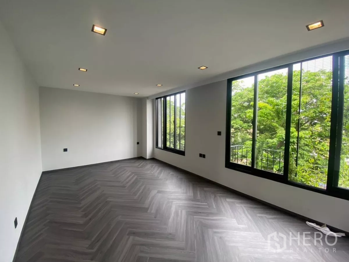 Townhouse for rent in Huai Khwang, Bangkok - Spacious bedroom with herringbone flooring and wide windows facing green trees.