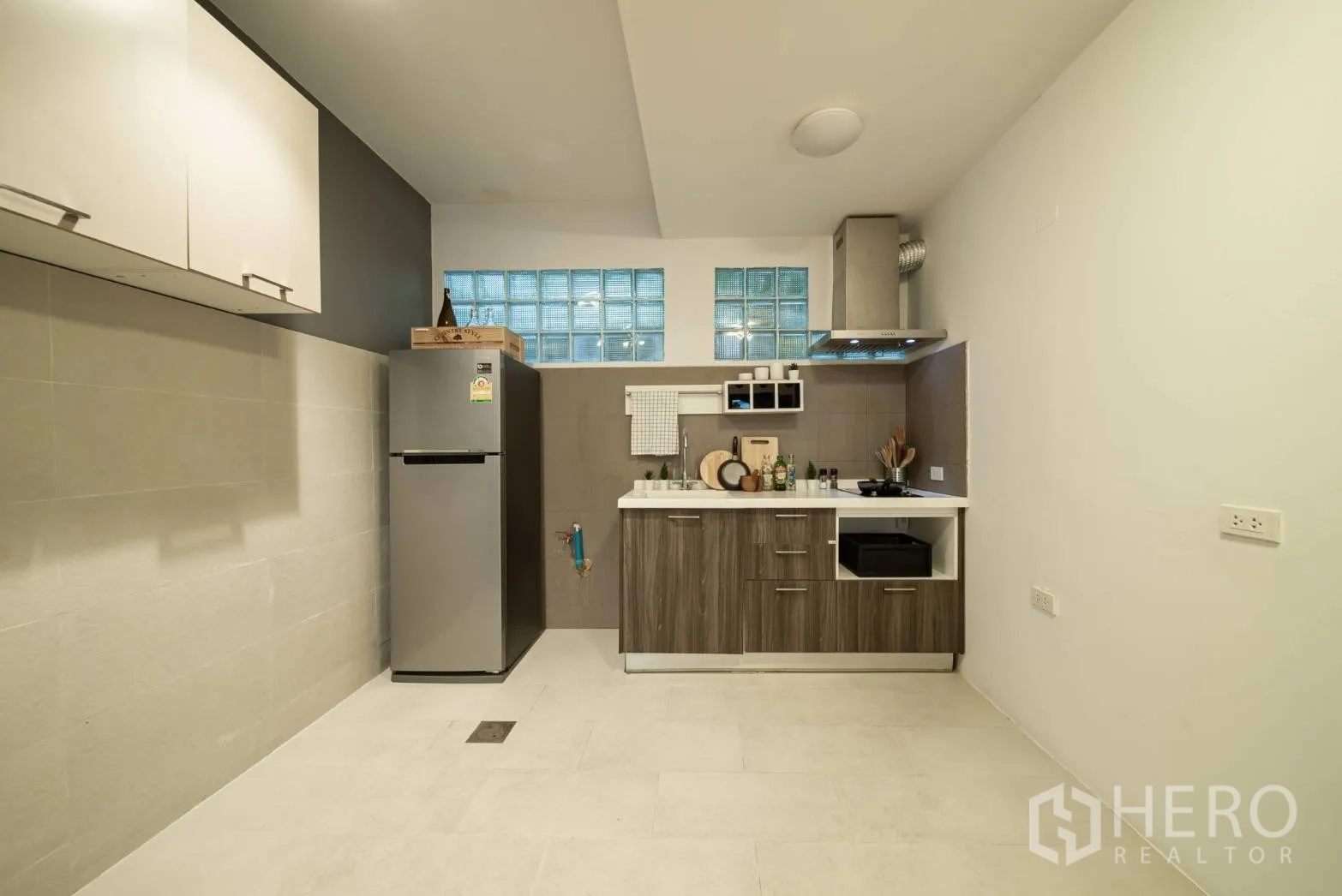 Townhouse for rent in Watthana, Bangkok - Compact modern kitchen with fridge, cooktop, vent hood and glass-block windows.