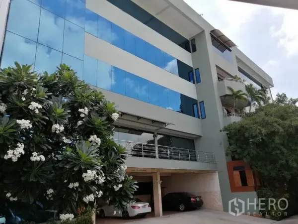 办公空间 出租在Bueng Kum, Bangkok - 现代化办公楼外立面，蓝色玻璃幕墙与绿树。