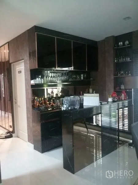 独立式住宅 出售在Nonthaburi - 内置备餐柜与吧台，黑色亮面柜体和镜面层架。