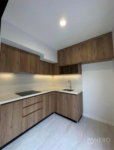 Townhouse for rent in Yan Nawa, Bangkok - L-shaped kitchen with wood cabinetry, electric hob and under-cabinet lighting.