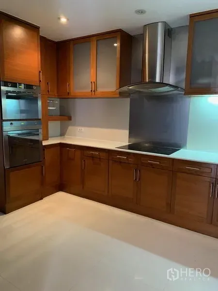 Condominium for sale in Khlong Toei, Bangkok - Modern kitchen with wooden cabinetry, range hood, cooktop and built-in oven.