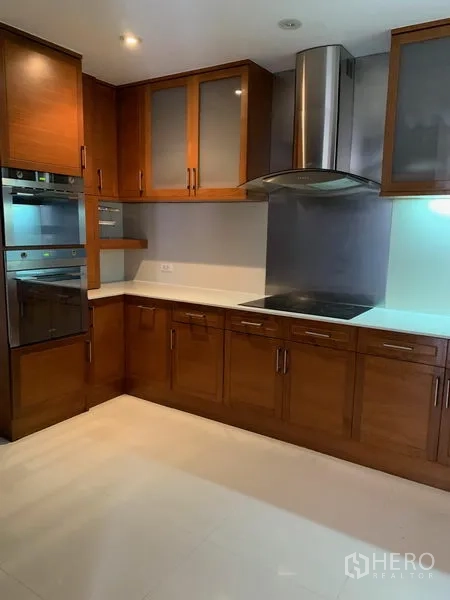 Condominium for sale in Khlong Toei, Bangkok - Modern kitchen with wooden cabinetry, range hood, cooktop and built-in oven.
