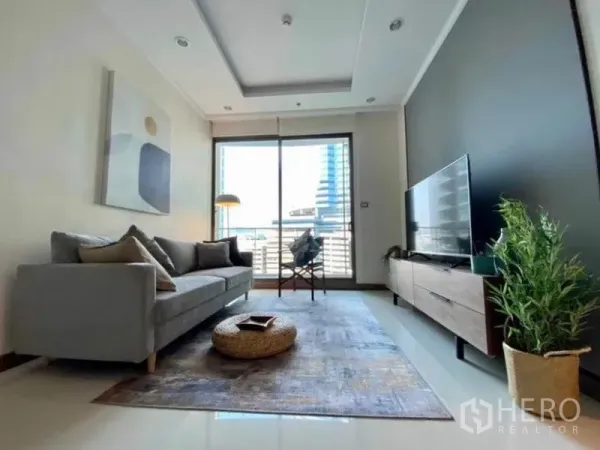 Condominium for rent in Watthana, Bangkok - Living room opening to a balcony with city view, TV console and large windows.