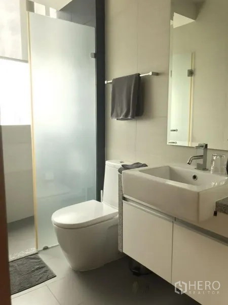 Condominium for rent in Khlong Toei, Bangkok - Bathroom with toilet, vanity, and frosted glass shower enclosure.