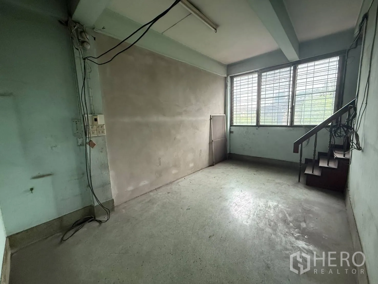Shophouse for rent in Khlong Toei, Bangkok - Bright room with barred windows and a staircase corner.