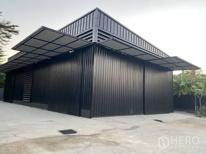 Warehouse for rent in Wang Thonglang, Bangkok - Modern black metal-clad warehouse exterior with large canopy over loading area and concrete yard.