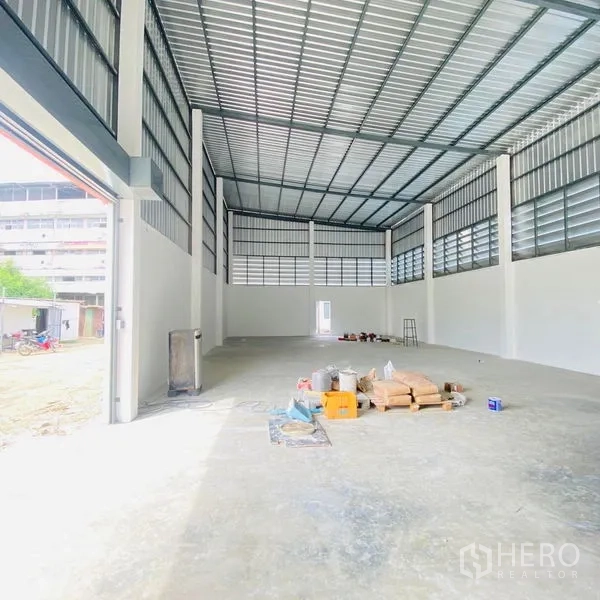 Warehouse for rent in Bang Khae, Bangkok - High‑clearance warehouse bay with wide roller entry, ventilated panels and materials on the floor.
