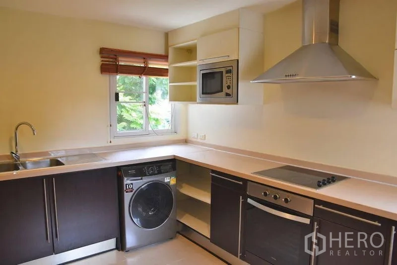 Apartment for rent in Sathon, Bangkok - U‑shaped kitchen with window, built‑in oven, cooktop, hood and washer.