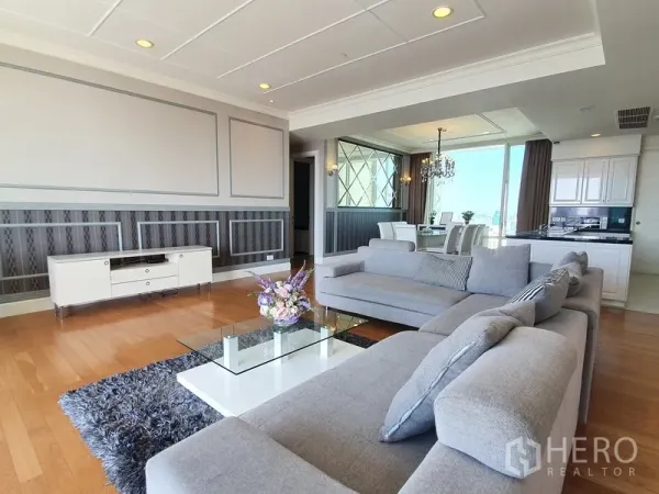 Condominium for rent in Watthana, Bangkok - Bright living room with grey sectional sofa, glass coffee table, wood floors, and open-plan dining beside a modern kitchen.