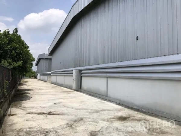 货栈 出租在Lat Lum Kaeo, Pathum Thani - 仓库侧立面，混凝土通道与绿化围栏