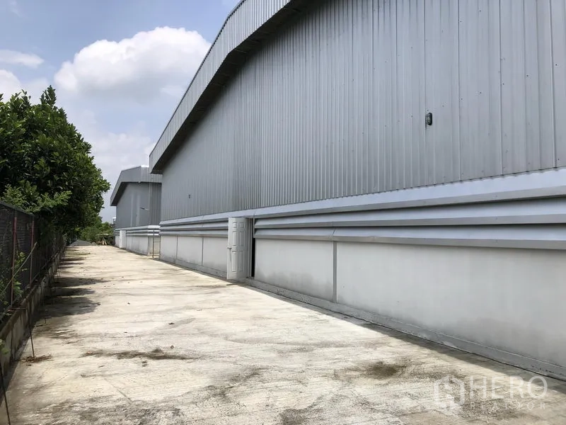 货栈 出租在Lat Lum Kaeo, Pathum Thani - 仓库侧立面，混凝土通道与绿化围栏