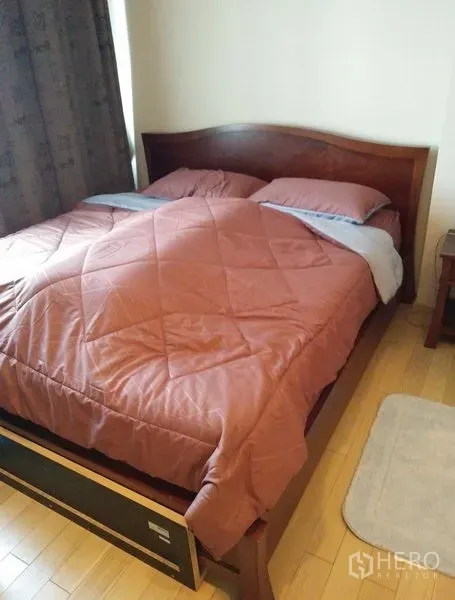 Condominium for rent in Khlong Toei, Bangkok - Cozy bedroom with a wooden bed frame, quilted duvet and light wood flooring.