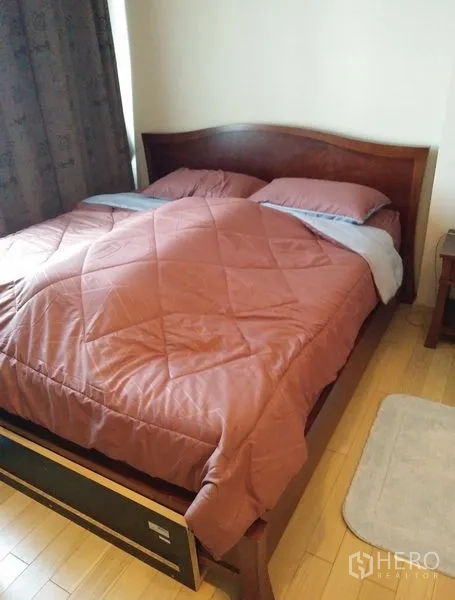 Condominium for rent in Khlong Toei, Bangkok - Cozy bedroom with a wooden bed frame, quilted duvet and light wood flooring.