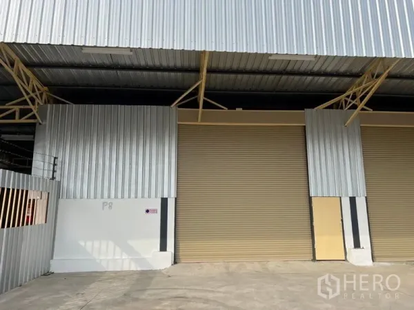 Warehouse for rent in Suan Luang, Bangkok - Metal-clad warehouse exterior with two beige roller shutter doors and a covered loading bay.