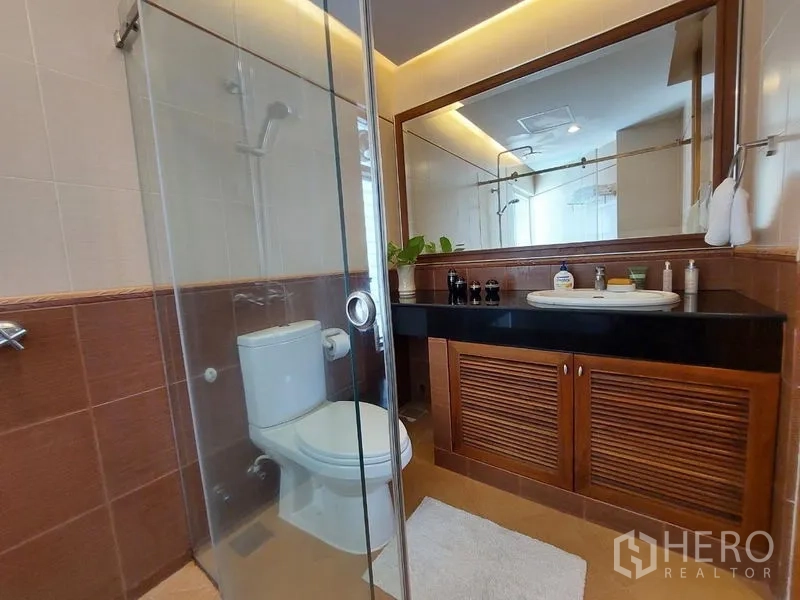 Apartment for rent - Bathroom featuring glass-enclosed shower, toilet, long black countertop and large mirror.