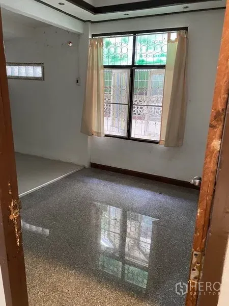 Townhouse for rent in Lat Phrao, Bangkok - Empty living area with polished terrazzo floor and curtained window with security grilles.
