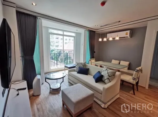 Condominium for rent in Sathon, Bangkok - Bright lounge with sofa, dining set and floor-to-ceiling doors opening to a leafy balcony.