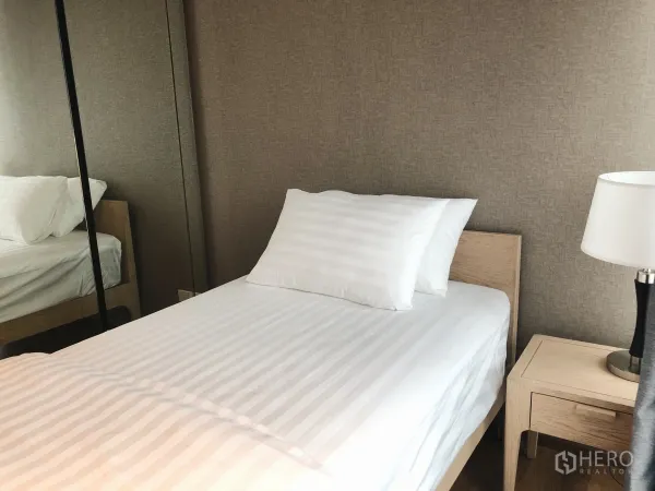 Condominium for rent in Khlong Toei, Bangkok - Compact second bedroom with single bed, bedside lamp and mirrored wardrobe.