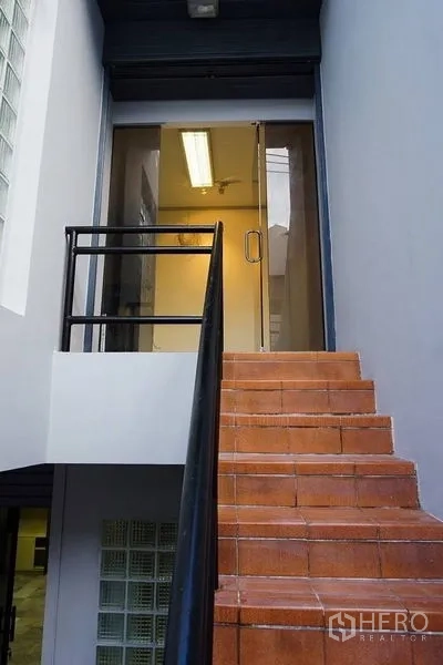 Home Office for rent in Khlong Toei, Bangkok - Exterior staircase with terracotta tiles leading to a secure glass entry door and grey walls.