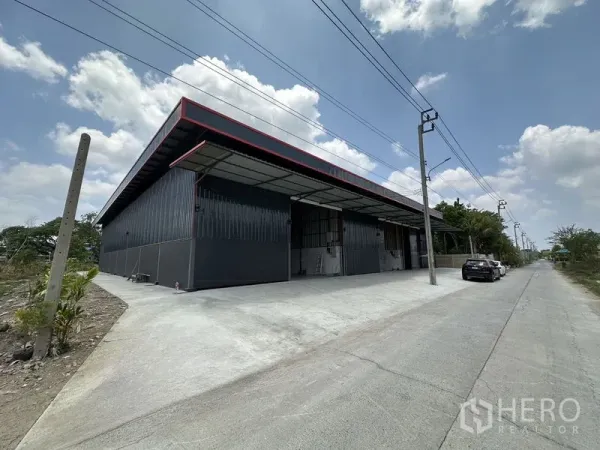 Warehouse for rent in Khlong Sam Wa, Bangkok - Exterior perspective of the warehouse beside a service road with parking space.
