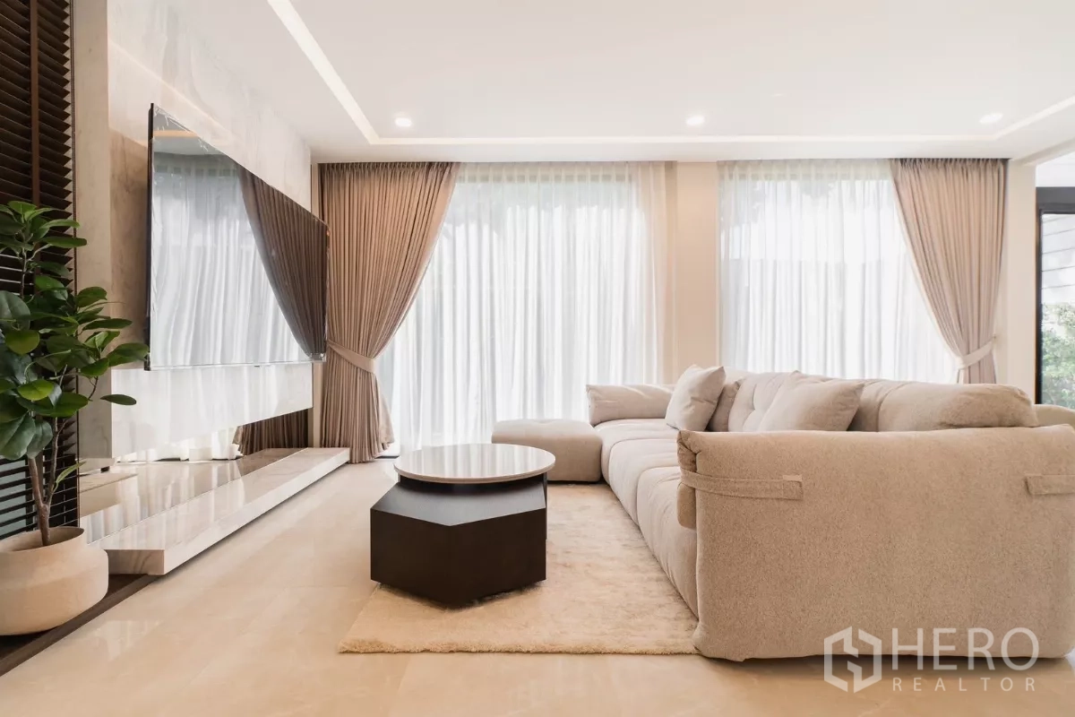Detached House for rent or sale in Prawet, Bangkok - Living area with large TV on marble feature wall, sheer curtains and recessed lights