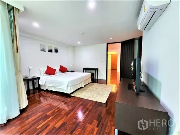 Condominium for rent in Bang Rak, Bangkok - Wide master bedroom with white walls, split air conditioner, TV stand and dark hardwood flooring.