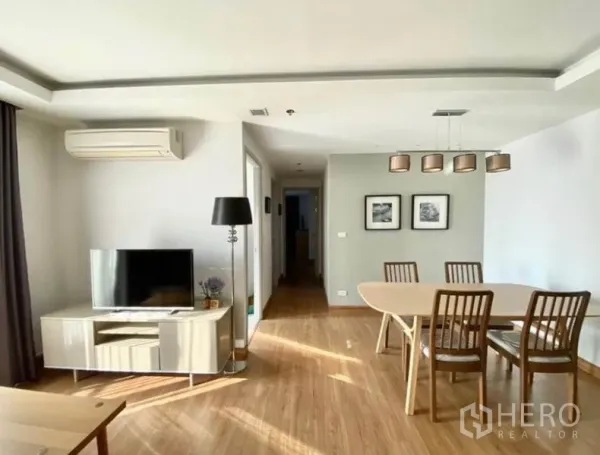 Condominium for rent in Huai Khwang, Bangkok - Open-plan lounge and dining room with TV, floor lamp and hallway leading to bedrooms.