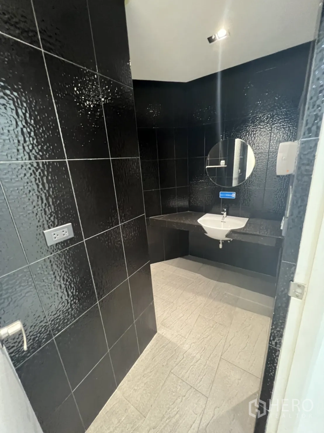 Retail Space for rent in Sathon, Bangkok - Bathroom with textured black wall tiles, round mirror and light floor.