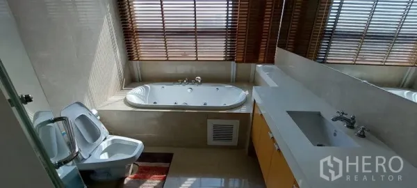 公寓 出租在Pathum Wan, Bangkok - 现代浴室，窗边浴缸，木百叶，长台面与大镜面，坐便器与坐浴盆。