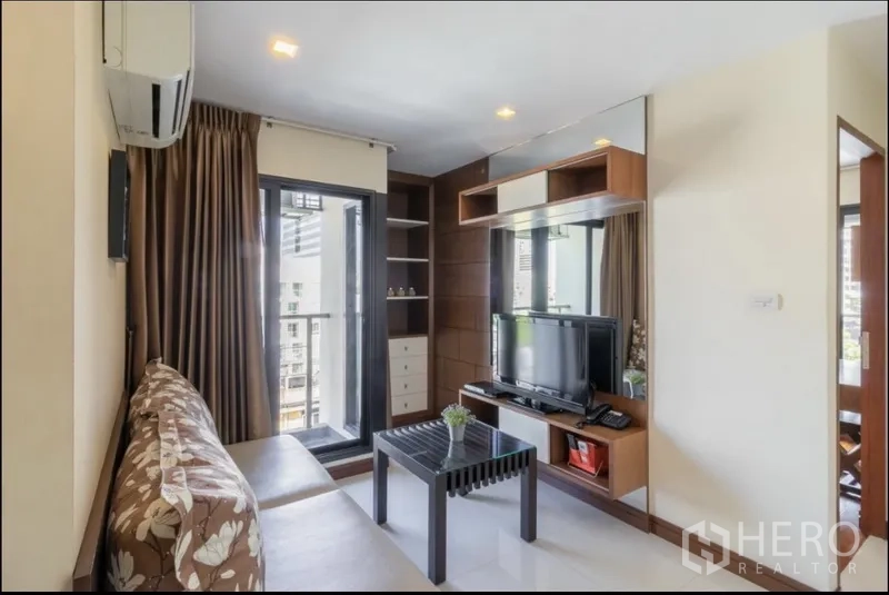 房间 出租在Bang Rak, Bangkok - 温馨客厅，大窗、茶几与墙面储物柜对着电视。