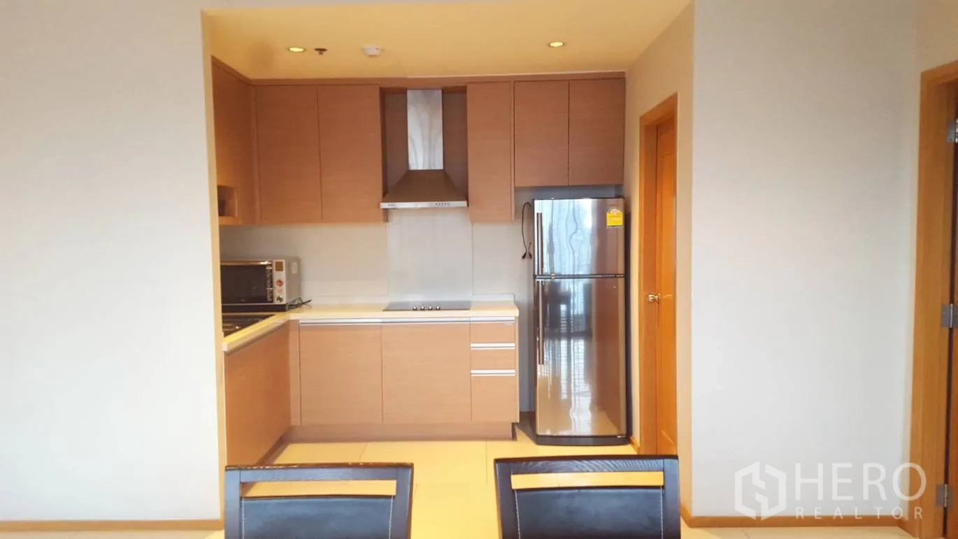 Condominium for rent or sale in Khlong Toei, Bangkok - Compact open kitchen with built-in wood cabinets, range hood and stainless refrigerator.
