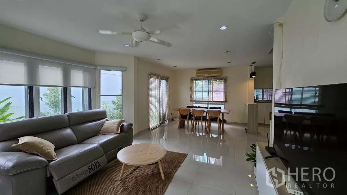 Detached House for rent in Khlong Toei, Bangkok - Bright open-plan living and dining area with leather sofa, TV wall, large windows and glossy tile floors.