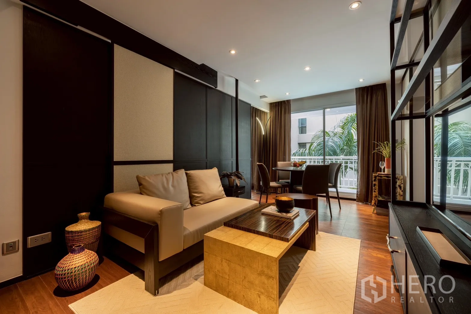 คอนโด for rent or sale in Pathum Wan, Bangkok - ห้องนั่งเล่นแบบโอเพ่นแพลน โซฟาสีครีม พื้นไม้ และวิวระเบียงร่มรื่น