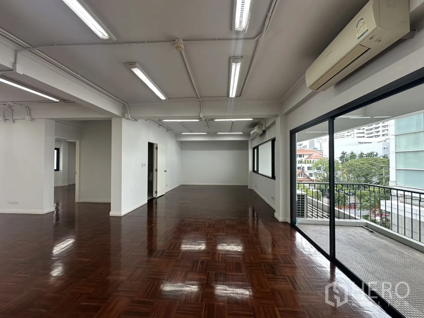 Office Space for rent in Watthana, Bangkok - Bright workspace with wall-mounted air conditioners, large windows, and balcony access.
